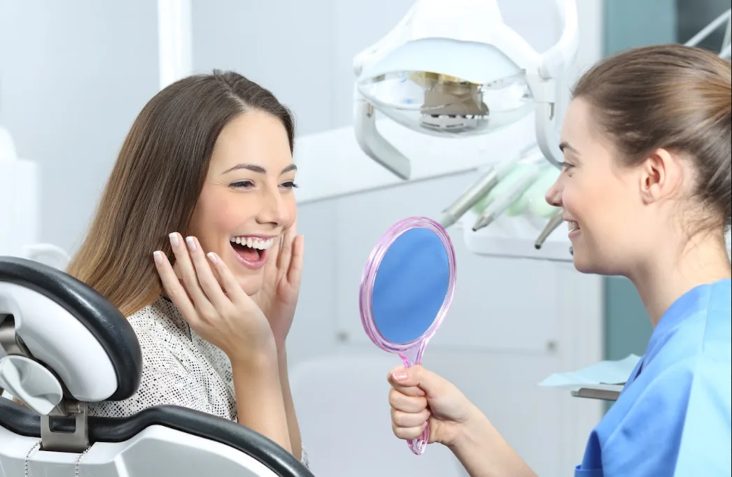 Patient smiling at her new smile in a hand mirror with her hygienist